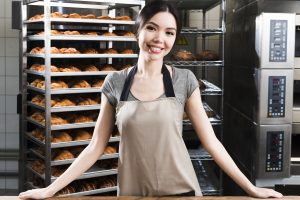 portrait-confident-young-female-baker-standing-front-baked-croissant-shelves