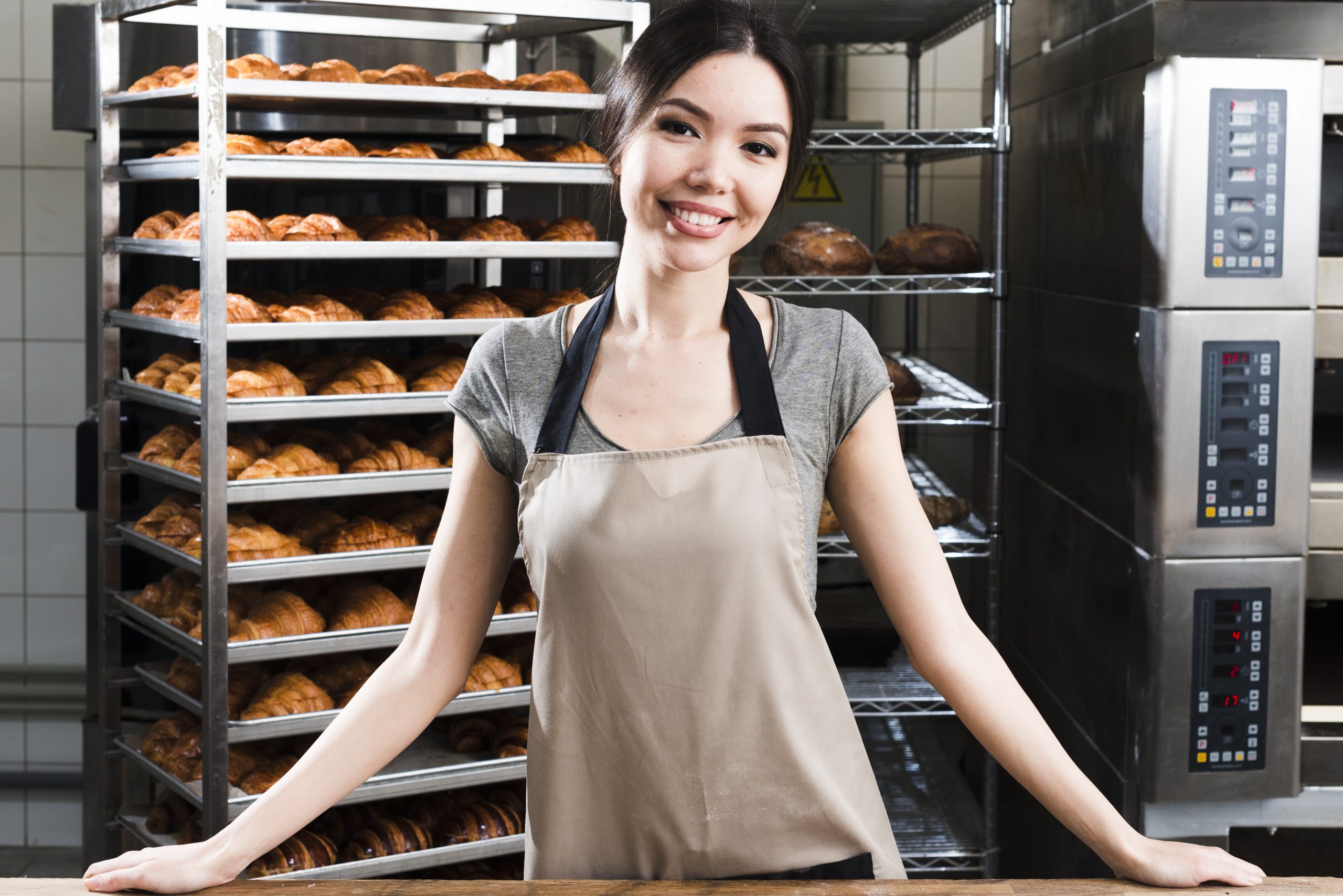 portrait-confident-young-female-baker-standing-front-baked-croissant-shelves