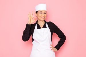front-view-young-female-cook-black-shirt-white-cook-cape-white-cap-posing-smiling-delighted