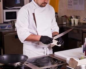 Portrait of a young chef cook in a hotel restaurant. Chef is cleaning a knife.
