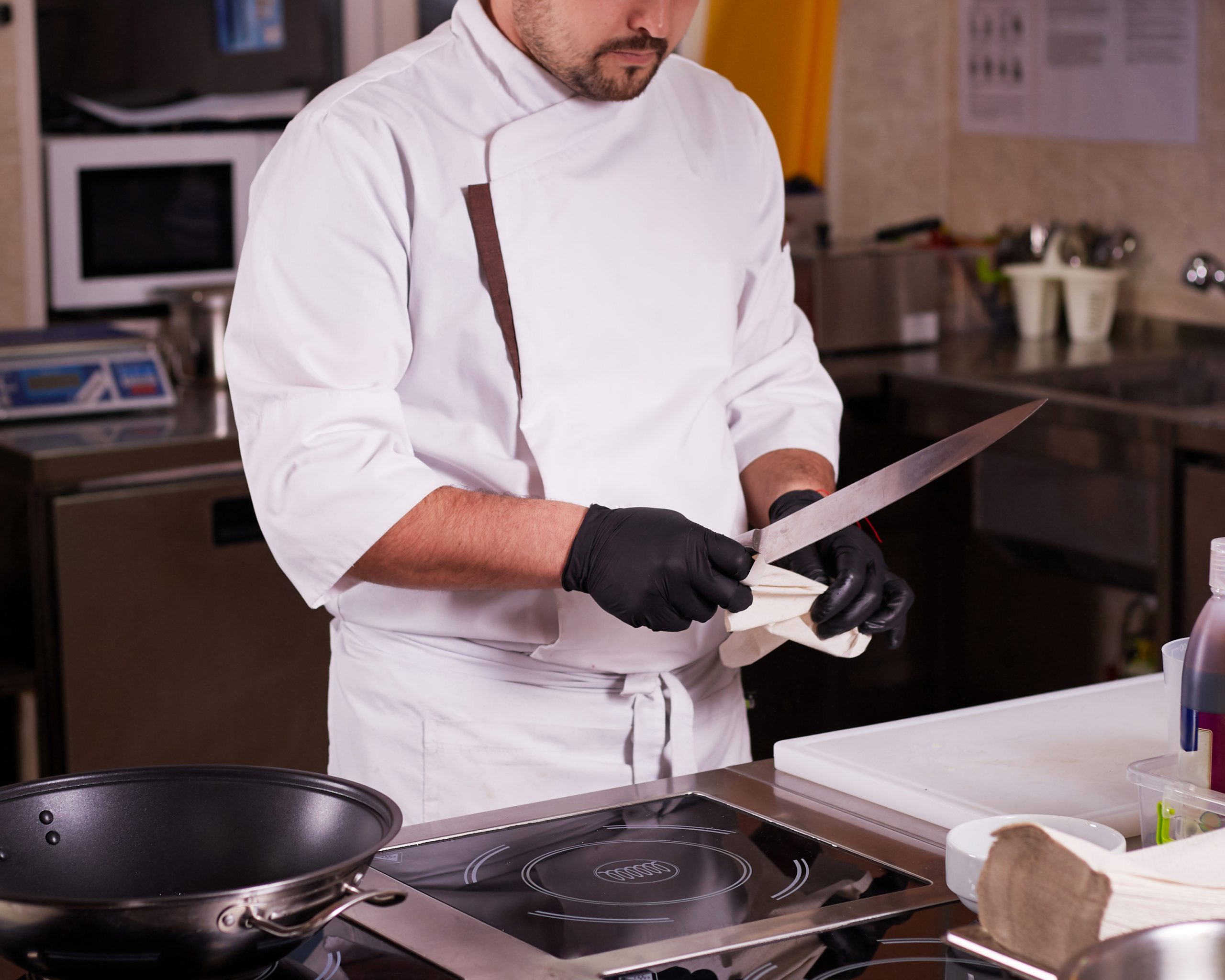 Portrait of a young chef cook in a hotel restaurant. Chef is cleaning a knife.
